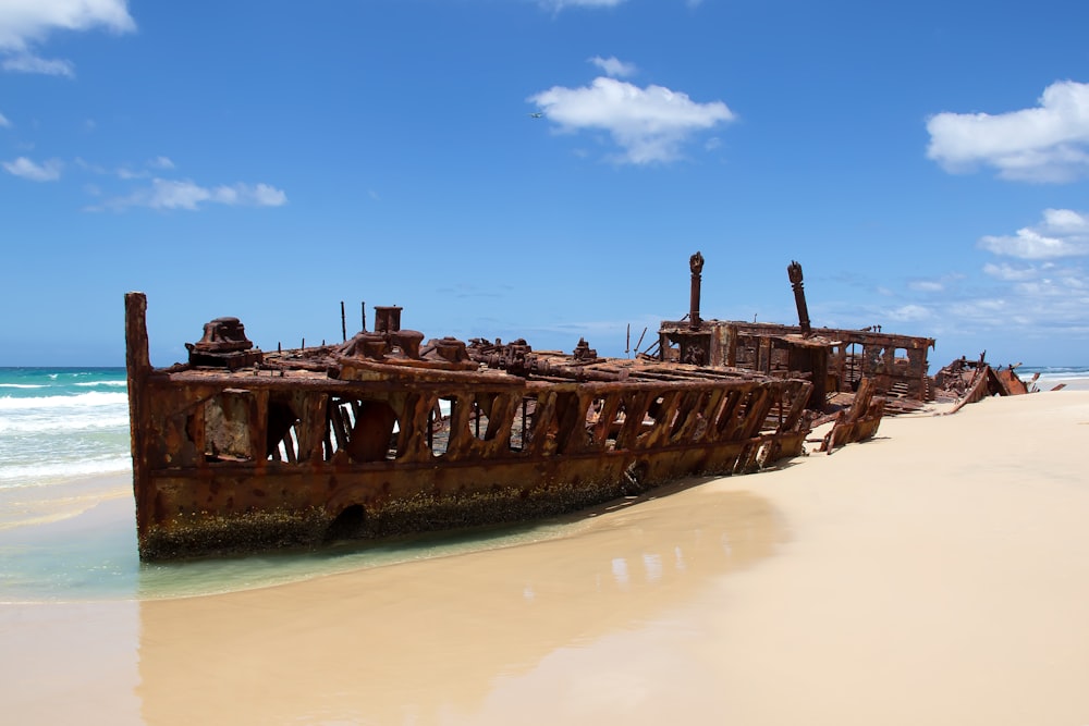 destroyed brown sailing boat near seashore under blue and white skies
