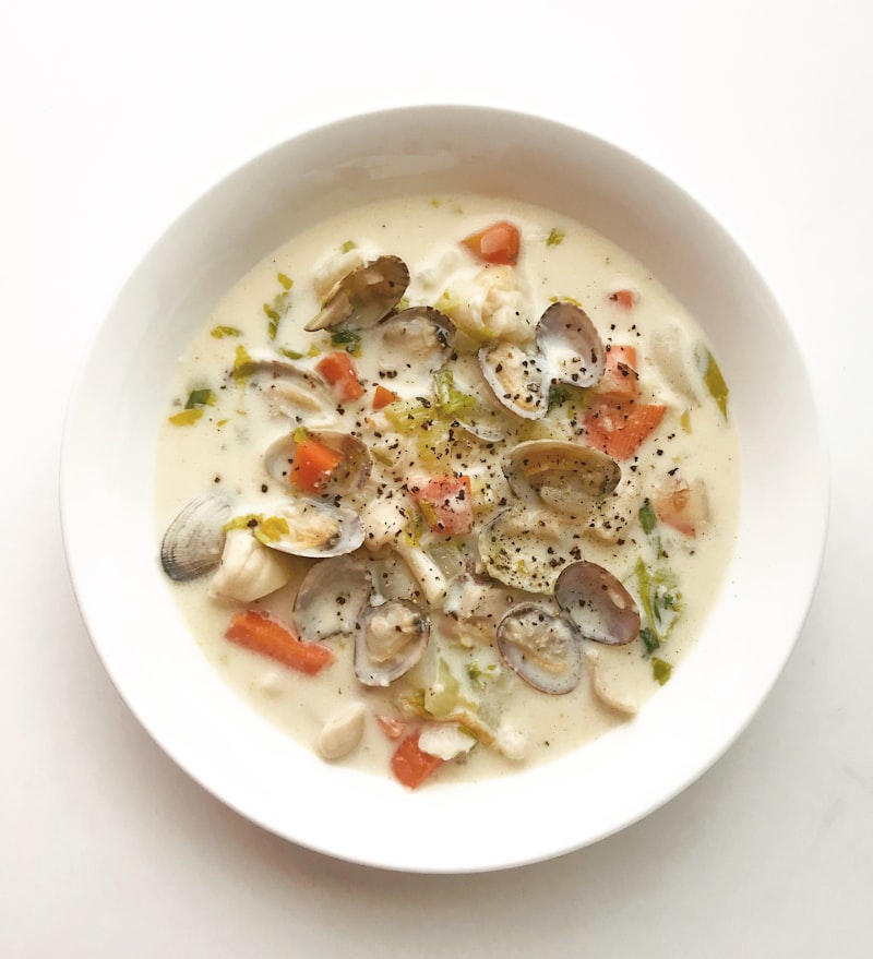 White bowl of clams in their shells in a light savory broth with vegetables
