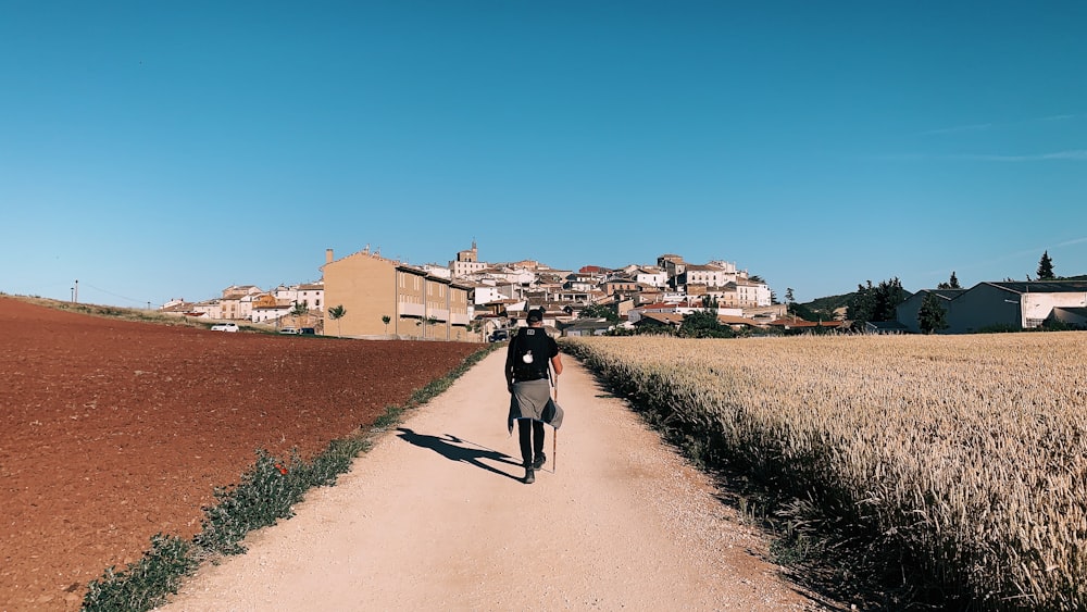 person in black shirt walking on dirt road between fields