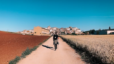 person in black shirt walking on dirt road between fields pilgrim teams background