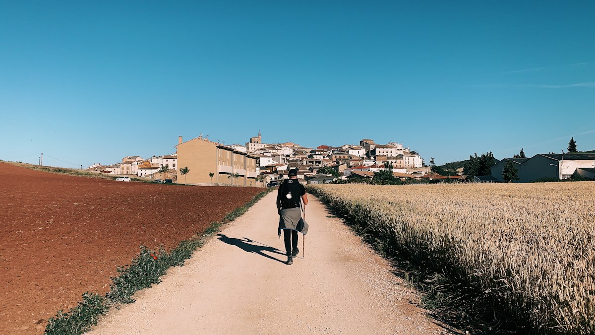 Persona caminando por un camino de tierra entre campos