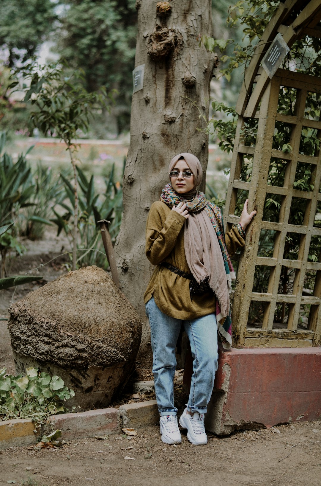 woman wearing brown long-sleeved shirt and gray headscarf leaning on tree