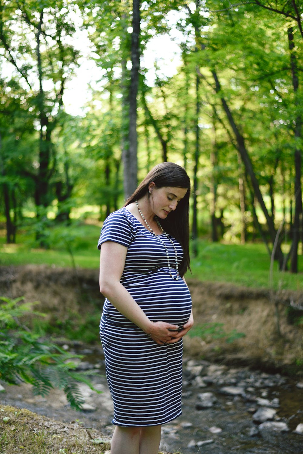 pregnant woman in white and black striped dress standing near river