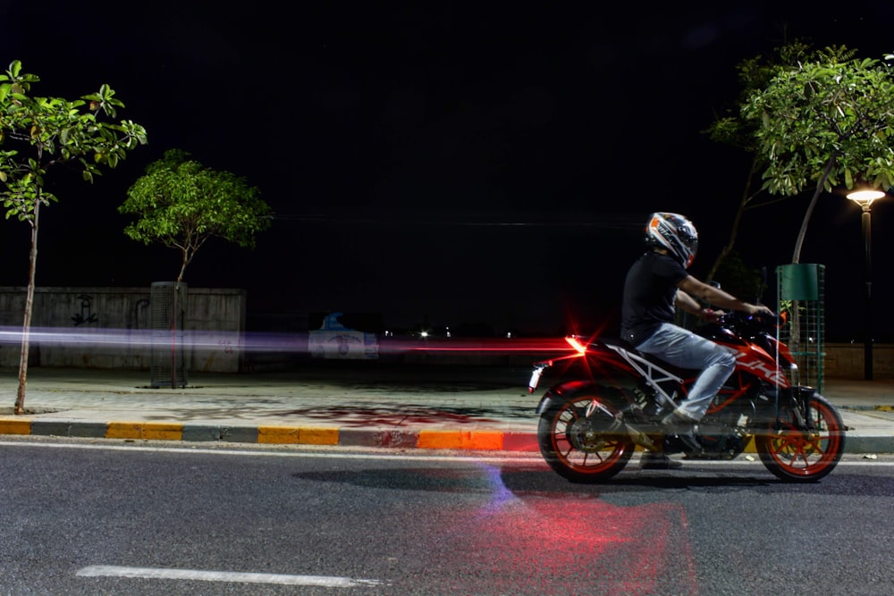 man riding red and black motorcycle on road during night time