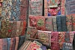 A vibrant array of richly embroidered and intricately patterned textiles are displayed, covering a wall with a variety of ornate designs. The fabrics feature a mix of geometric and floral motifs, with colors ranging from deep blues and reds to bright pinks and greens. Each textile appears to be hand-crafted with detailed stitching and unique patterns.