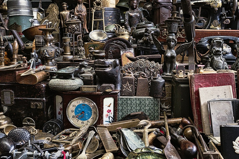 Amas d’objets anciens sur un étal de brocante : horloge, statuettes, cuivres et coffrets, illustration des brocantes d’octobre 2026 en Wallonie et à Bruxelles