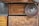 Various wooden surfaces and textures are visible, including panels and a circular object. The wood features natural grain patterns and a rich, warm tone.