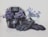 A motorcycle helmet filled with vibrant purple flowers sits beside a pair of black gloves. In the background, a container filled with the same type of flowers adds a decorative touch. The flowers contrast beautifully against the dark helmet and gloves, lending a soft yet striking appearance to the scene.