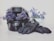 A motorcycle helmet filled with vibrant purple flowers sits beside a pair of black gloves. In the background, a container filled with the same type of flowers adds a decorative touch. The flowers contrast beautifully against the dark helmet and gloves, lending a soft yet striking appearance to the scene.