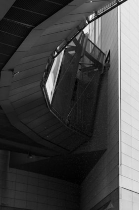 An architectural structure with angular and geometric elements, featuring a combination of metal and concrete materials. The perspective is upward, highlighting intricate lines and shadows created by the design.