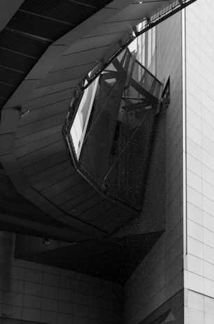 An architectural structure with angular and geometric elements, featuring a combination of metal and concrete materials. The perspective is upward, highlighting intricate lines and shadows created by the design.