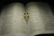 A gold ring rests on an open book, with its shadow forming a heart shape on the pages. The text on the book is in a language with a distinct script, possibly Malayalam.