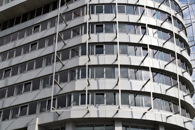 A modern multi-story building with a curved facade featuring rows of rectangular windows. The structure has an industrial appearance with vertical and horizontal lines created by metallic beams and panels.
