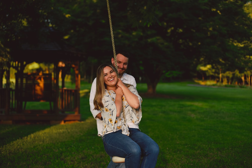 man standing behind smiling woman on swing