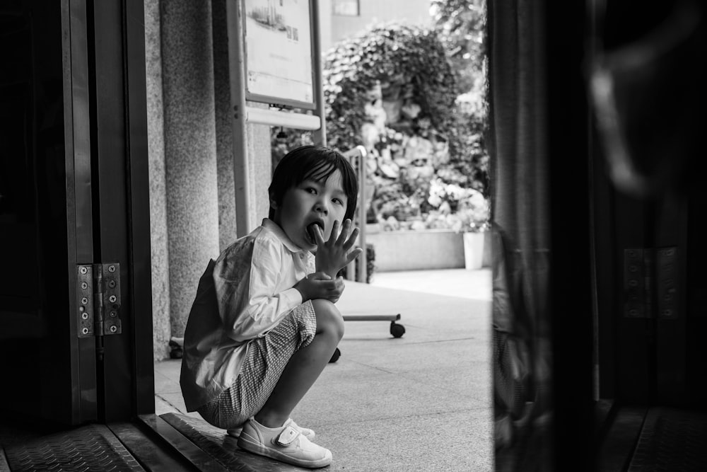 grayscale photography of boy sitting in front of door way