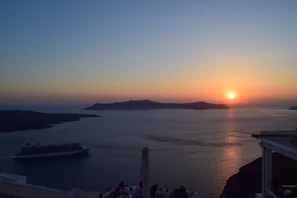 Sunset view over a calm ocean with a luxury cruise ship in the distance.