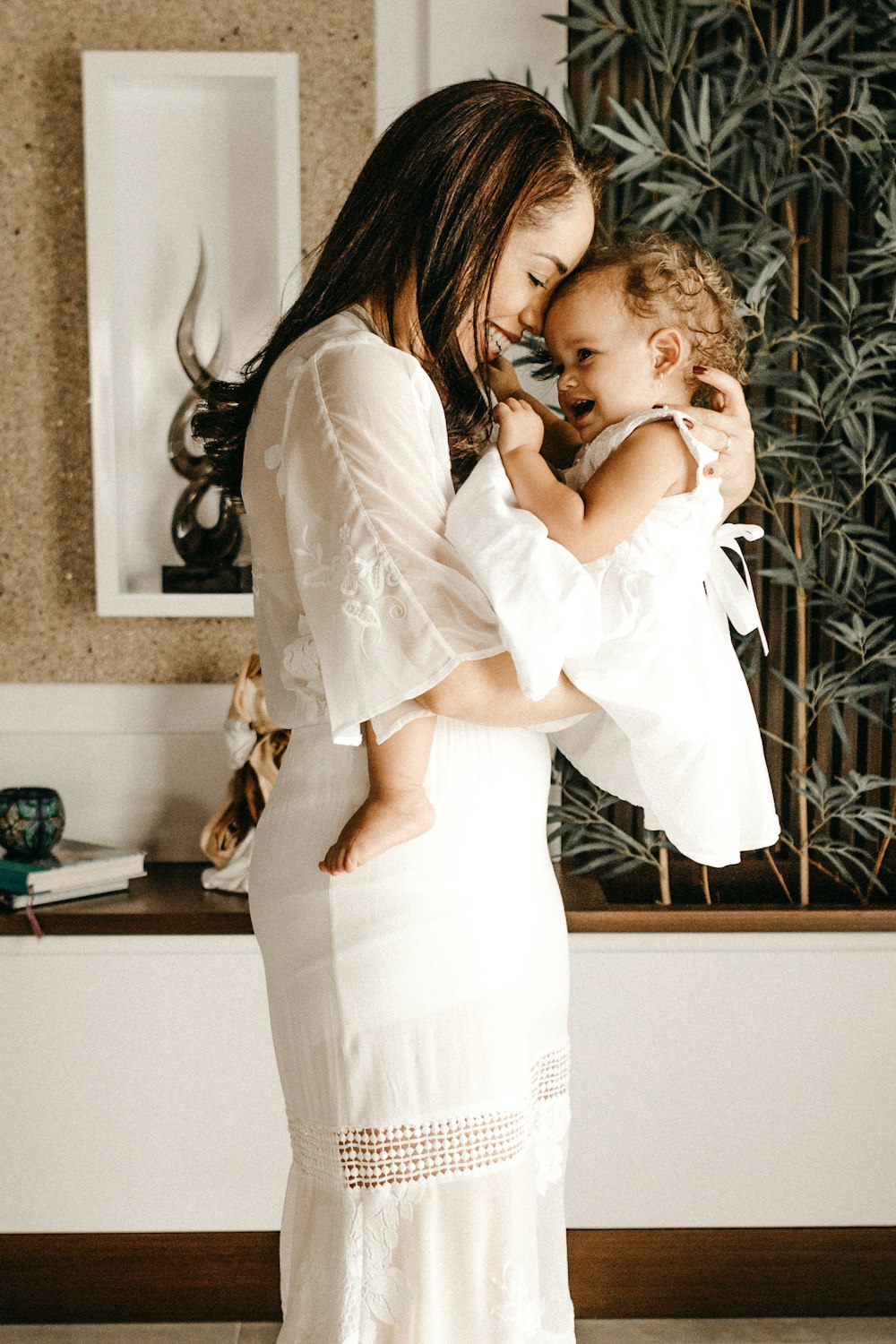 Lächelnde Frau im weißen Kleid hält Kleinkind