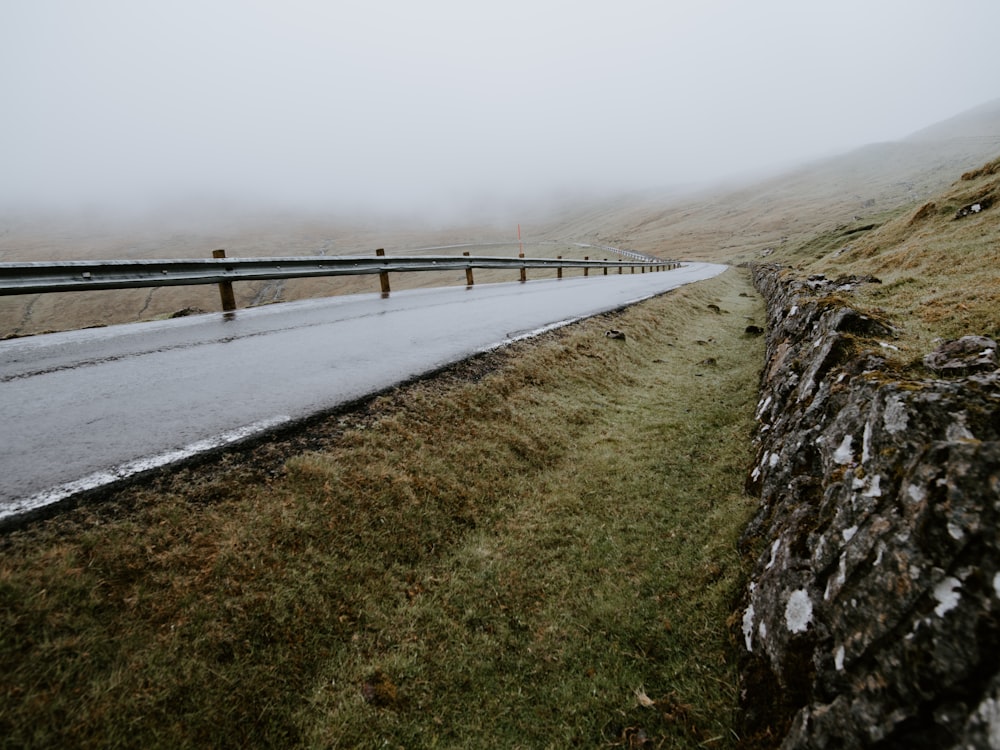 a wet road with a stone wall on the side of it