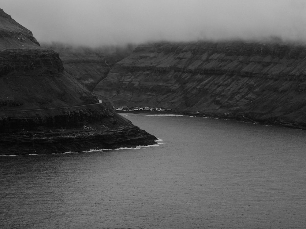 body of water between rocky mountain in grayscale photo