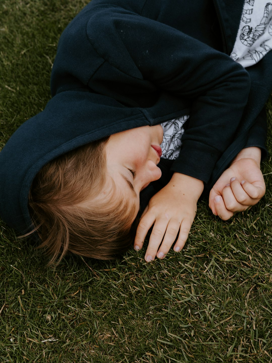 person wearing black pullover hoodie lying on grass