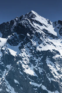 A majestic mountain peak dusted with snow under a clear blue sky, perfect for adventure seekers.