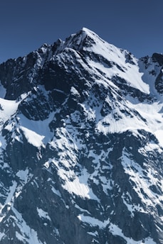 A majestic mountain peak with birds soaring above it against a clear blue sky.