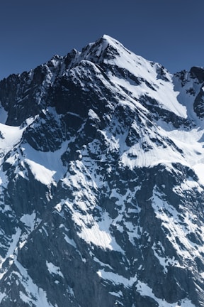 A majestic mountain peak dusted with snow under a clear blue sky.