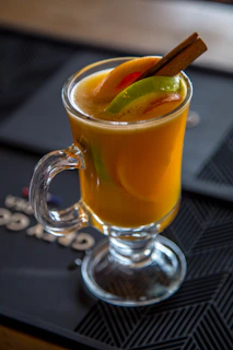 Bright orange mug filled with herbal tea surrounded by fresh herbs and citrus slices