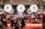 A lively bar scene with a warm, inviting atmosphere. Large circular light fixtures with the letters B, A, and R hang prominently above the counter. Several patrons are gathered around the bar, conversing and enjoying drinks. The bar itself is well-stocked with various liquors and glasses, and there are plants adding a touch of greenery to the space.