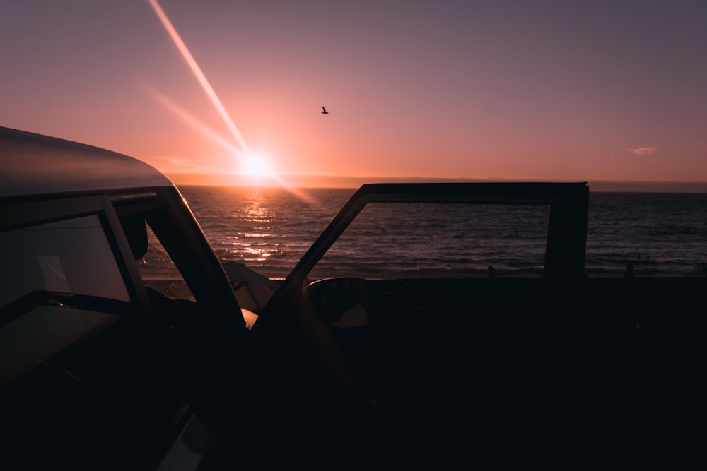 vehicle parked beside seashore during sunset