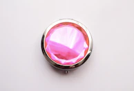 Close-up of hands holding a delicate pink compact mirror with the she unique logo.