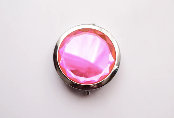 Hand holding a cute compact mirror with a sparkly pink cover reflecting soft natural light.