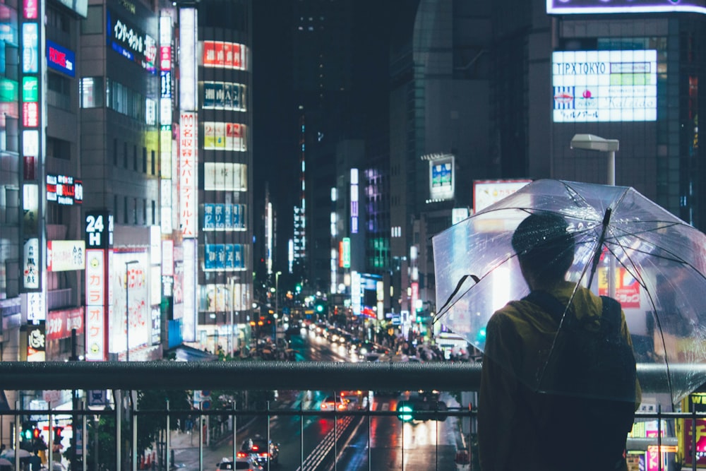 夜間に都市の建物を横切って透明な傘を持っている人