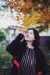 A cheerful international student standing in front of a Canadian college campus with autumn leaves.