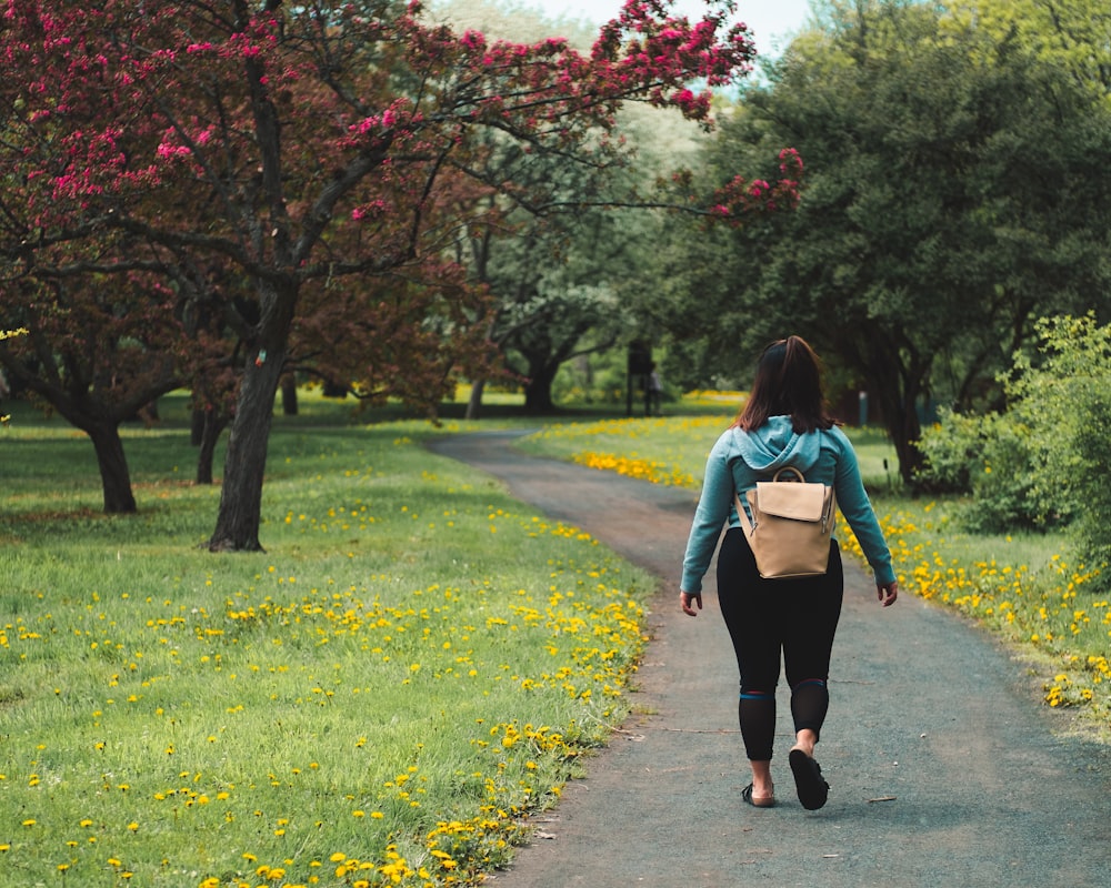 femme portant une veste bleue et un pantalon noir marchant sur un sentier de champ d’herbe