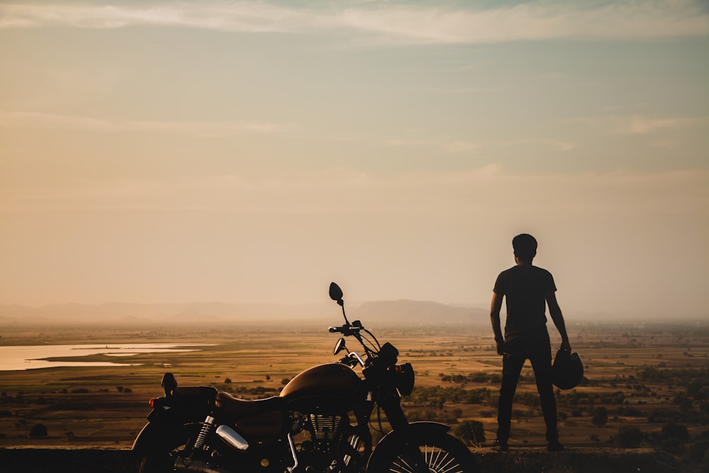 person standing besides motorcycle across grassland during dusk