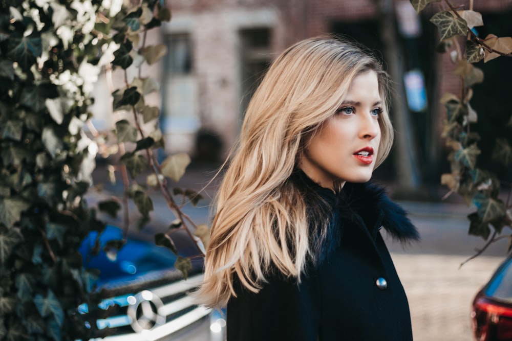 woman wearing black coat besides green vines photo