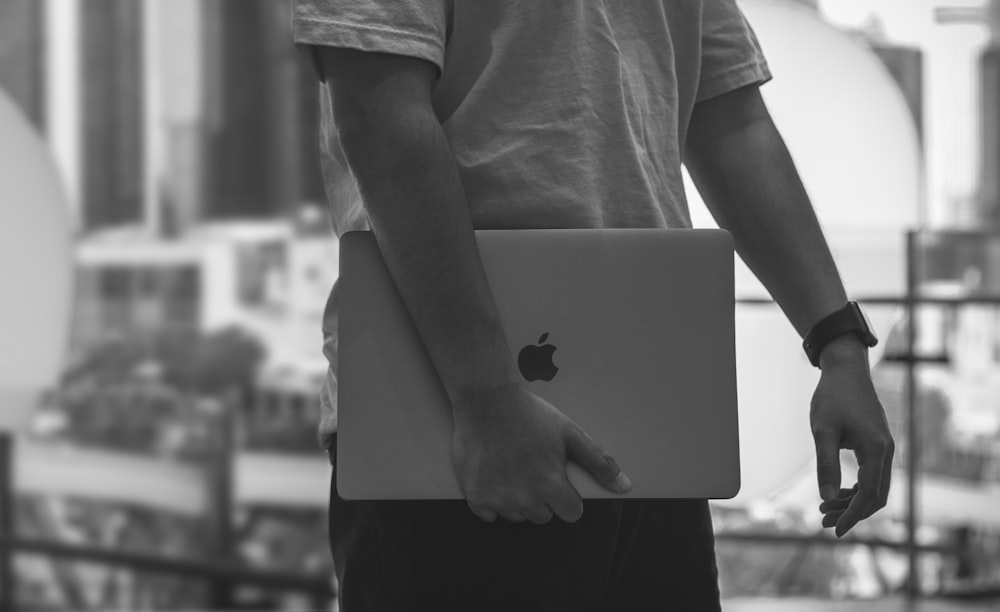 grayscale photo of a man carrying a Macbook