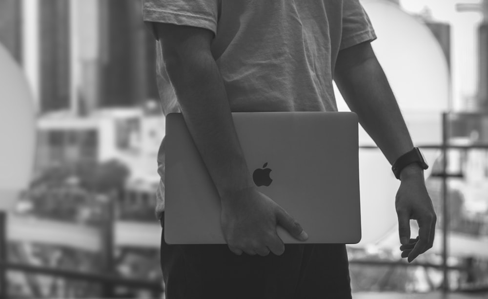 grayscale photo of a man carrying a Macbook