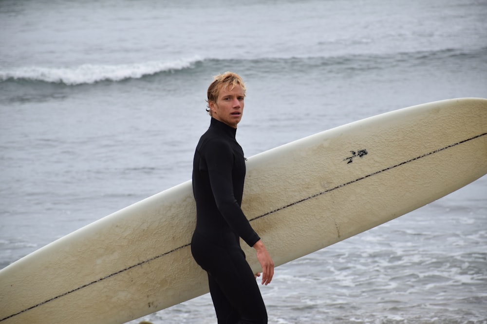 photography of man holding surfboard beside seashore during daytime