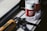A bottle of Nongfu Spring water with a red label sits on a surface next to a caulking gun. The scene is lit by natural light, casting distinct shadows and highlighting the textures of the objects.