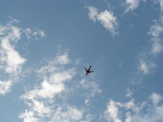 A vibrant airplane soaring above fluffy white clouds under a clear blue sky.