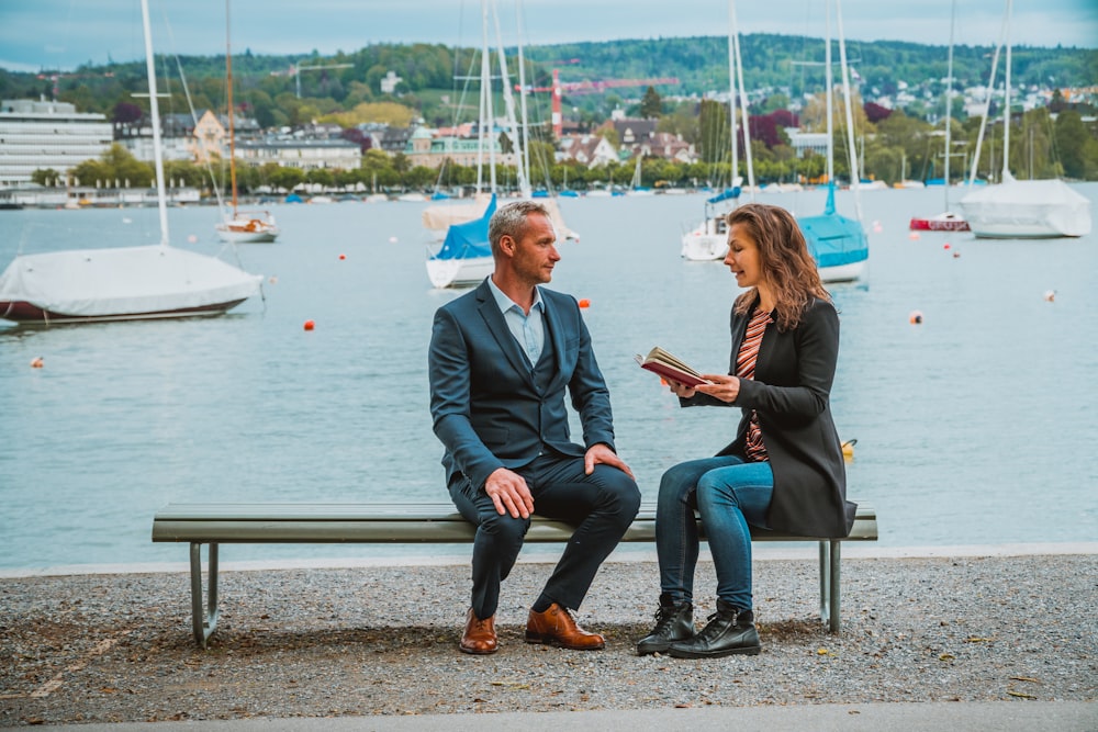 man sitting beside woman on bench near yacht boats