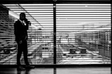 silhouette of man standing beside clear glass wall while using smartphone