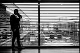 silhouette of man standing beside clear glass wall while using smartphone