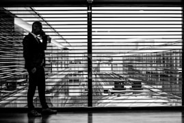 silhouette of man standing beside clear glass wall while using smartphone