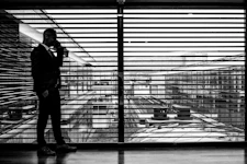 silhouette of man standing beside clear glass wall while using smartphone