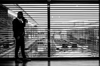 silhouette of man standing beside clear glass wall while using smartphone