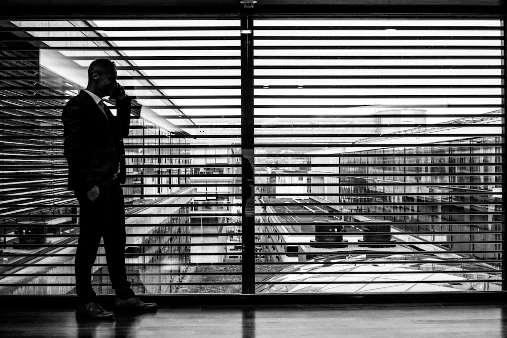 silhouette d’homme debout à côté d’un mur de verre clair tout en utilisant un smartphone