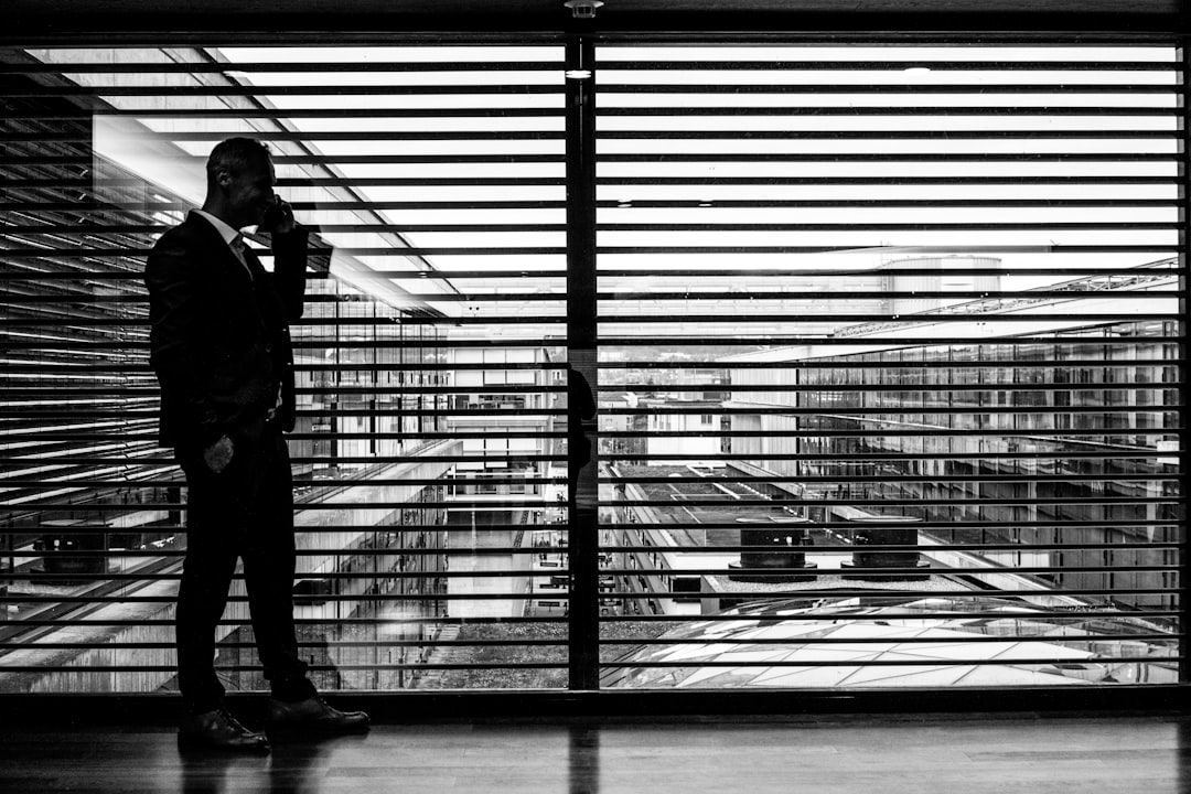 silhouette of man standing beside clear glass wall while using smartphone, business man